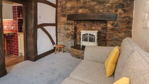 A cozy living room with a stone fireplace, wooden beams, and a grey sofa with a yellow pillow. - The Coach House (Holywell)