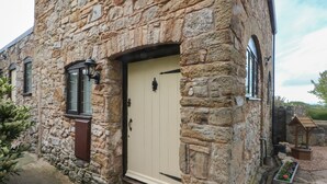 A stone building with a beige door, a small window with a black frame, and a lantern on the wall. - The Coach House (Holywell)