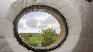A circular window with a view of a green landscape and trees. - The Coach House (Holywell)