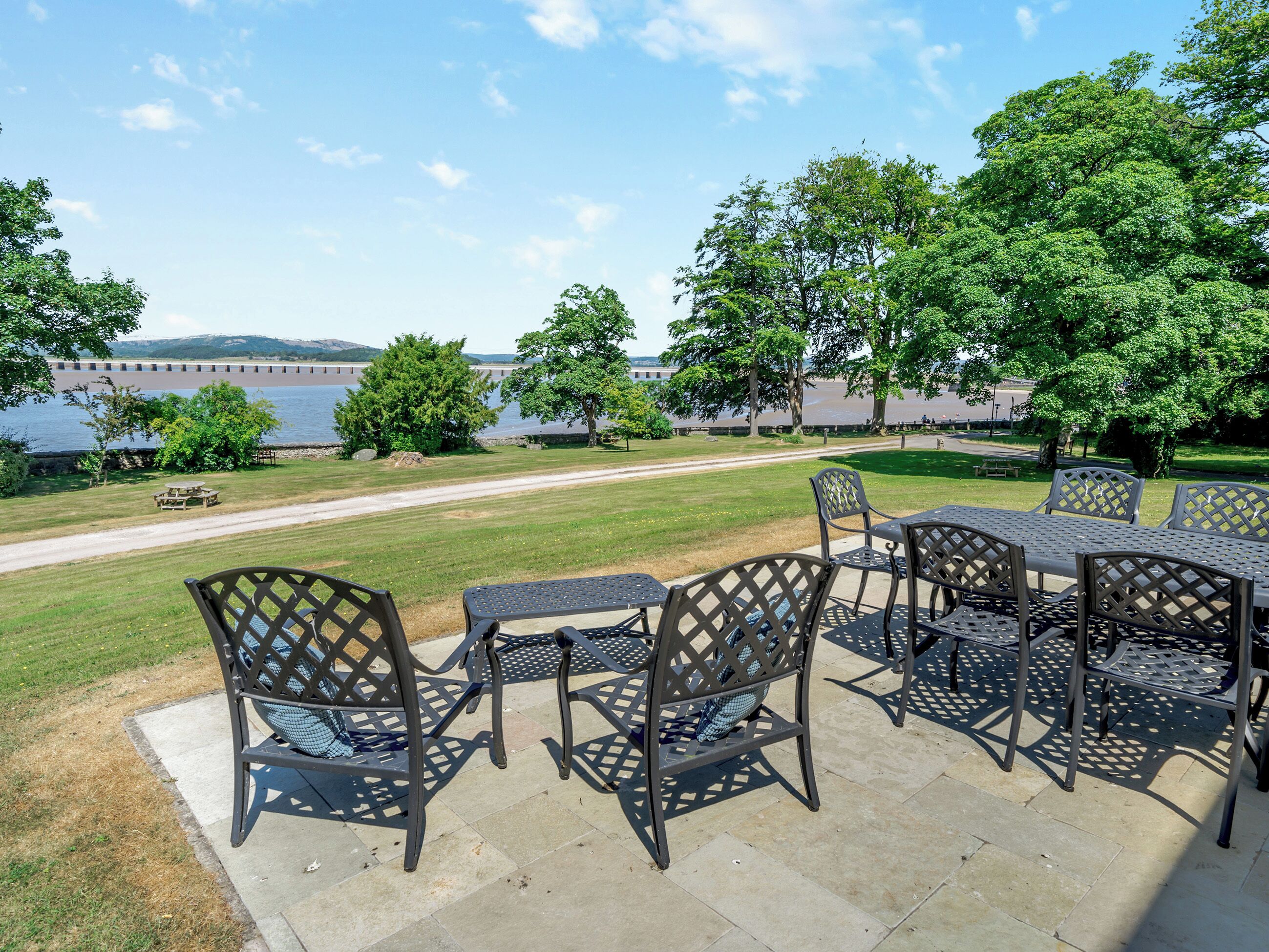 An outdoor patio with metal chairs and tables, a grassy area, and a view of a lake and dam in the background.