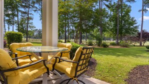 A patio with a glass table and yellow chairs, surrounded by a lawn and trees. - World Tour Golf Course overlooking the greens. Spacious 2 Bed 2 Bath on the 9th. (Myrtle Beach)