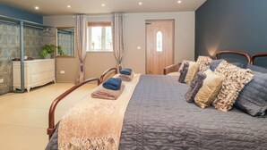 A bedroom with a bed, a dresser, a mirror, a window with curtains, and a door. - Yarn Cottage (Broadway)