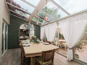 A dining area with a glass enclosure, wooden furniture, and a table set for four. - Yarn Cottage (Broadway)