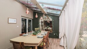 A dining area with a table set for six, surrounded by wooden chairs with green cushions. - Yarn Cottage (Broadway)