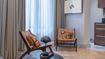 Een moderne woonkamer met twee rieten fauteuils, een ronde salontafel en een aan de muur bevestigde televisie.
