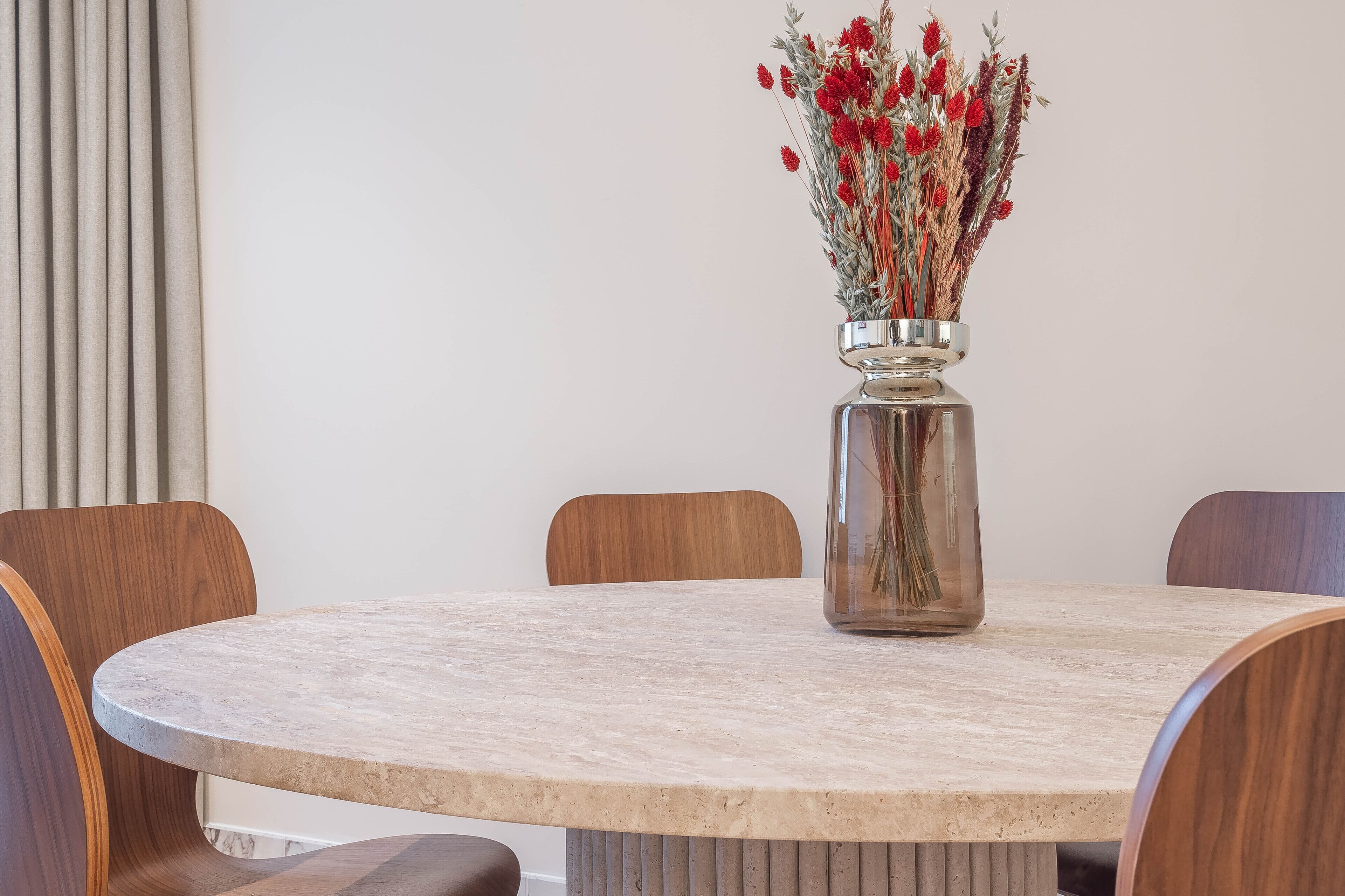 Une table de salle à manger ronde, ornée d’un vase rempli de fleurs rouges.