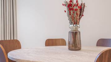 Une table de salle à manger ronde, ornée d’un vase rempli de fleurs rouges.