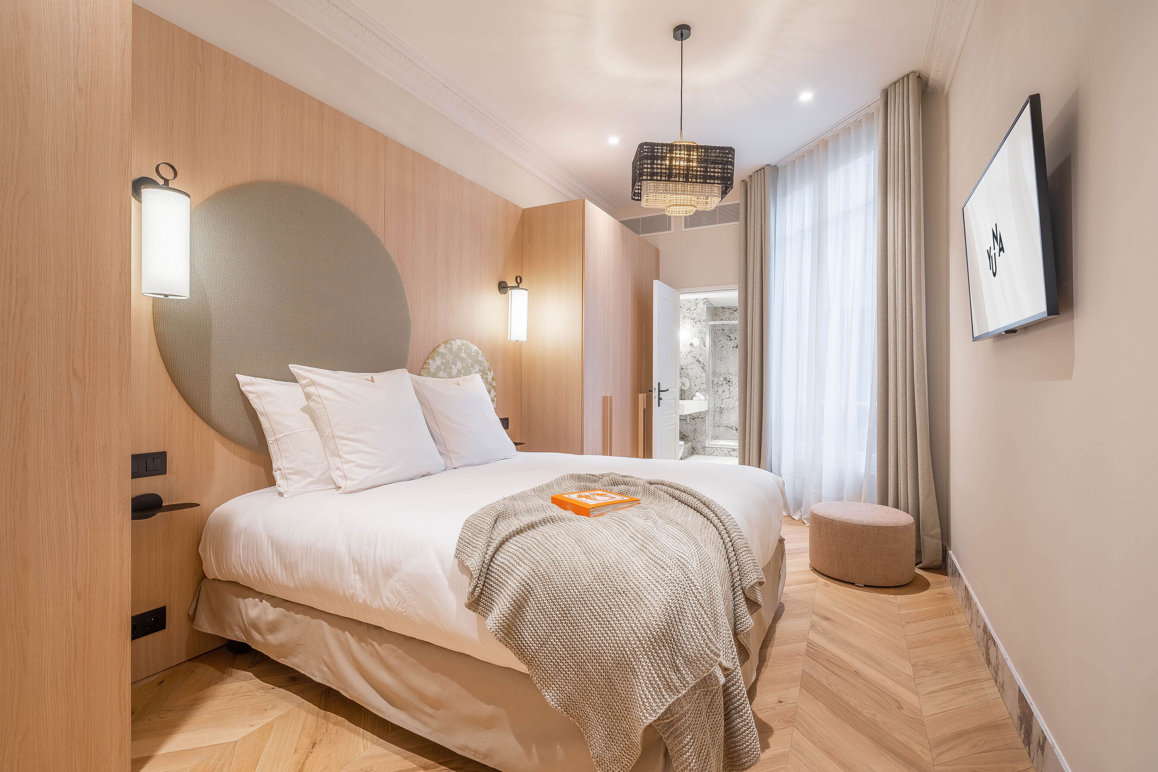 A modern bedroom with a large bed, bedside lamps, a round mirror, and a television on the wall.