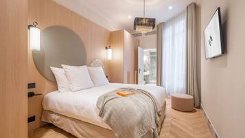 A modern bedroom with a large bed, bedside lamps, a round mirror, and a television on the wall.