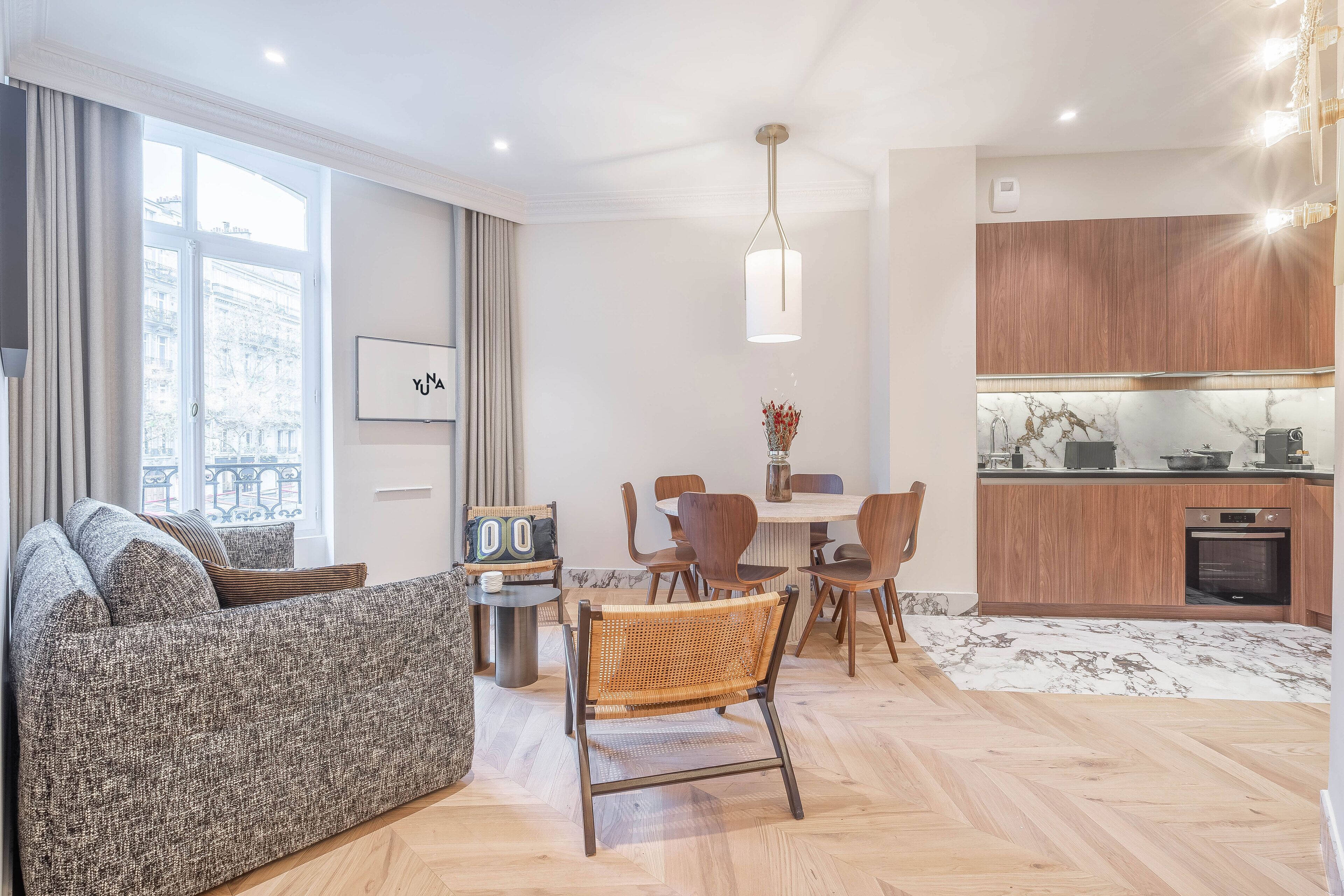 Una sala de estar moderna con sofá, mesa de comedor, sillas y una cocina con armarios de madera y encimera de mármol.