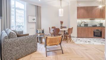 Una sala de estar moderna con sofá, mesa de comedor, sillas y una cocina con armarios de madera y encimera de mármol.