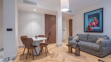 A modern living room with a round dining table, wooden chairs, a grey patterned sofa, and a framed poster on the wall.