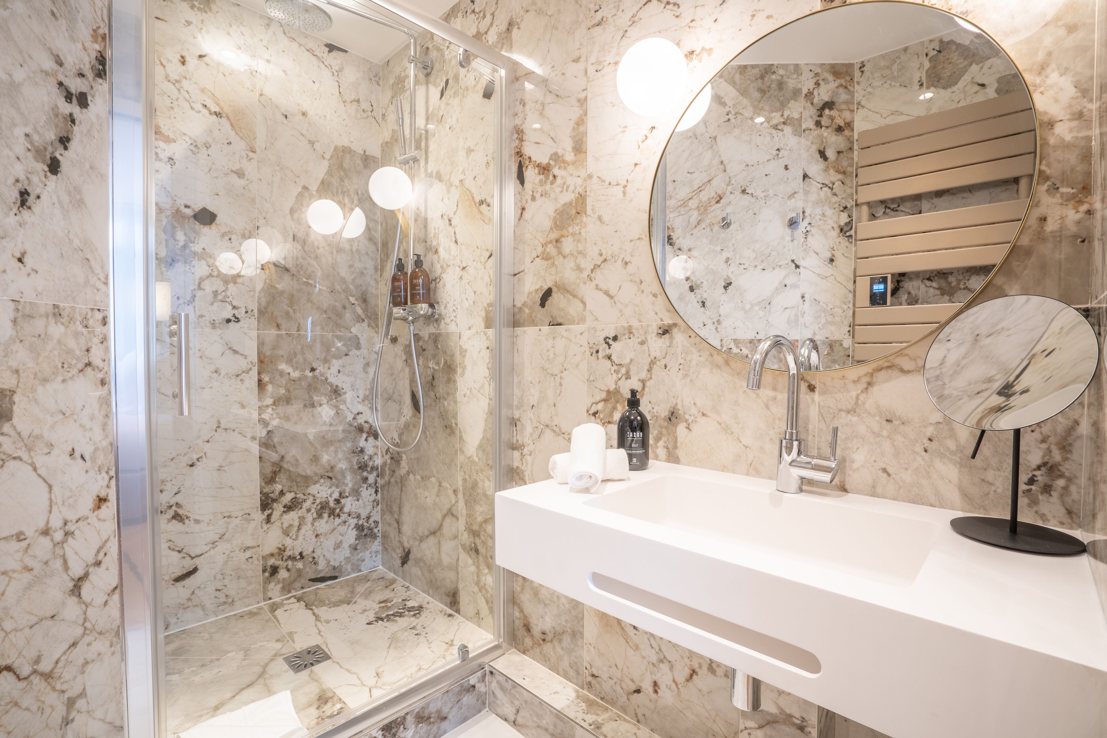 Un bagno moderno con doccia in marmo, uno specchio grande e un lavandino bianco.