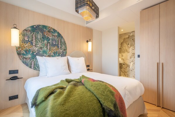 Une chambre moderne avec un grand lit, deux lampes fixées au mur, une œuvre d’art murale de forme circulaire et une armoire en bois.