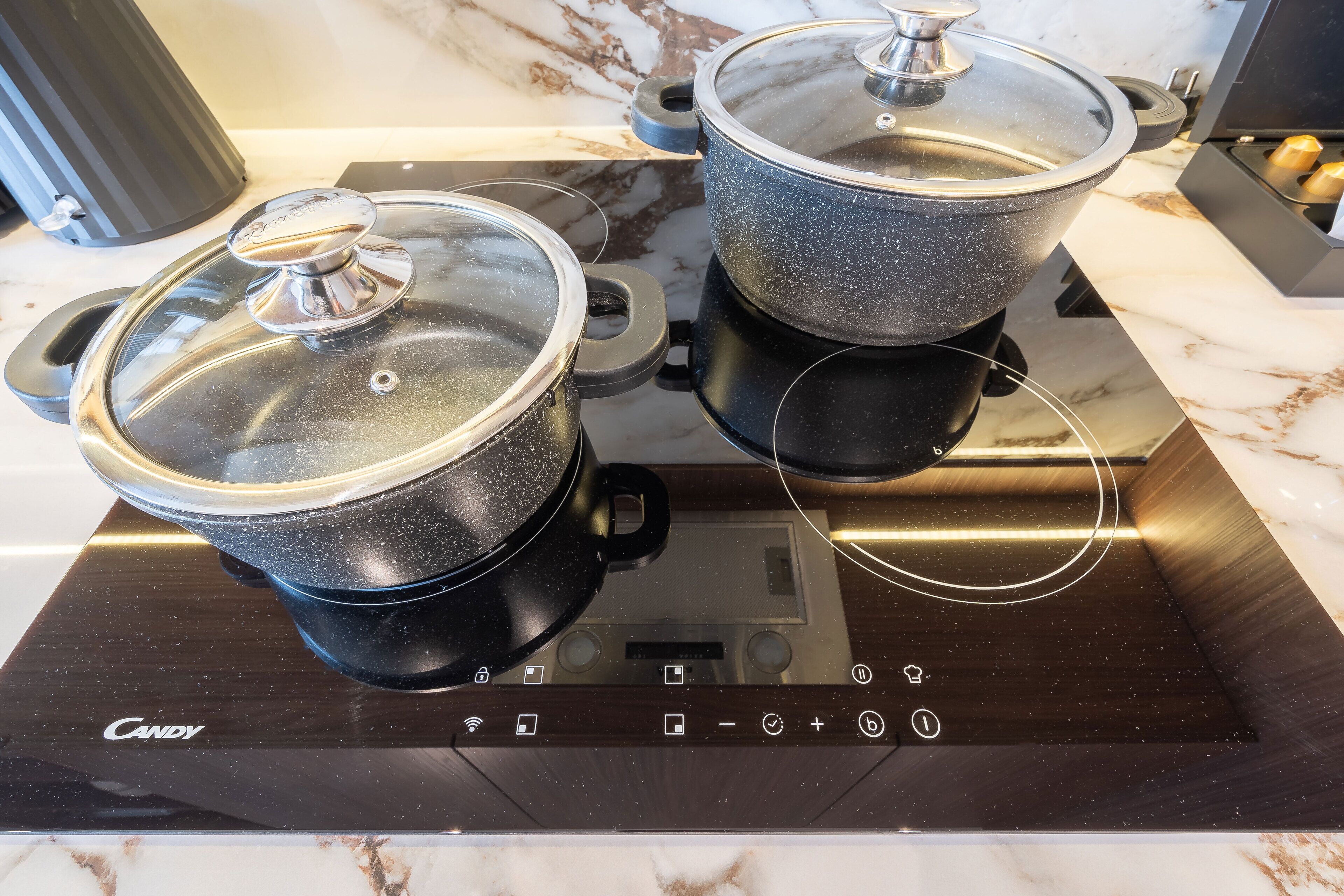 Two pots on a modern induction cooktop with a control panel.
