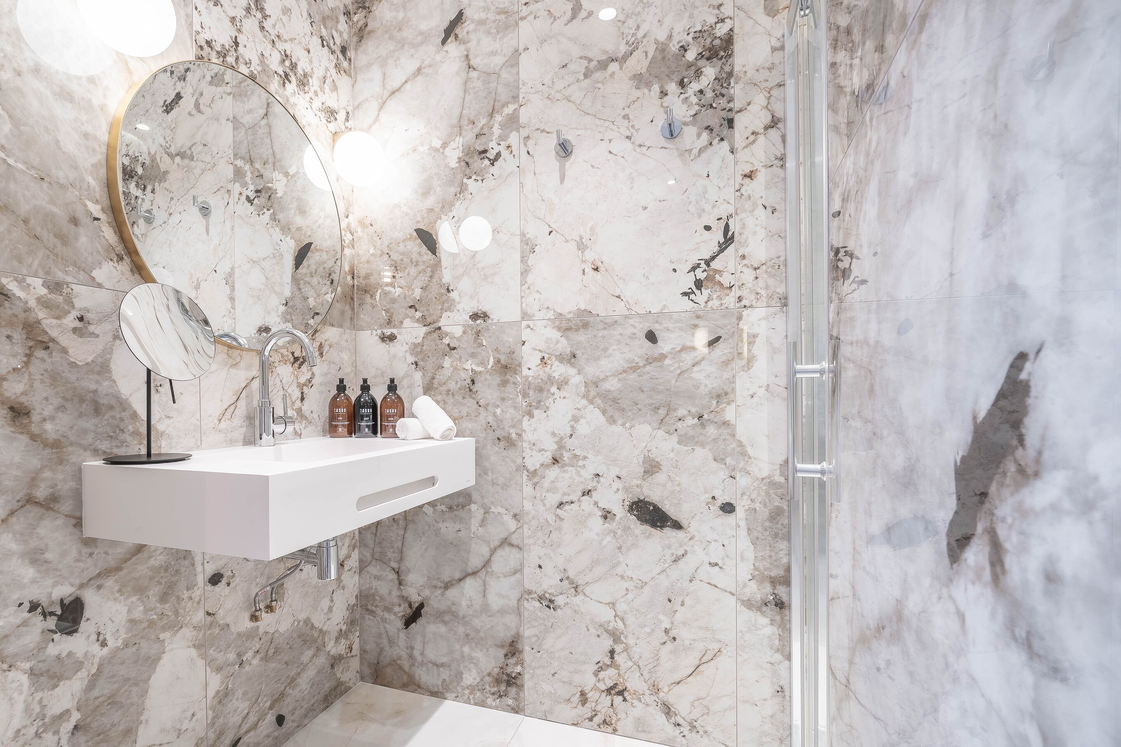 Ein modernes Badezimmer mit Marmor-Spritzschutz, einem weißen Waschbecken mit Spiegel und einer Duschkabine aus Glas.