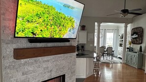 Ein Wohnzimmer mit einem Flachbildfernseher an einem Steinkamin, einer Holzzieldecke und Blick in den Essbereich.