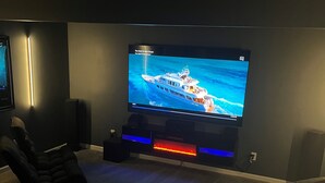 Ein Heimkino mit einem großen Flachbildfernseher an der Wand, einer gemütlichen Sitzecke mit bequemen Sesseln und einem Teppichboden.