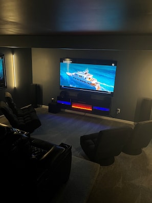 Une salle de cinéma privée équipée d’un grand téléviseur à écran plat fixé au mur, d’un espace salon confortable avec des fauteuils moelleux et d’un sol recouvert de moquette.