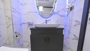 Un baño con lavamanos blanco, mueble negro y paredes de mármol.