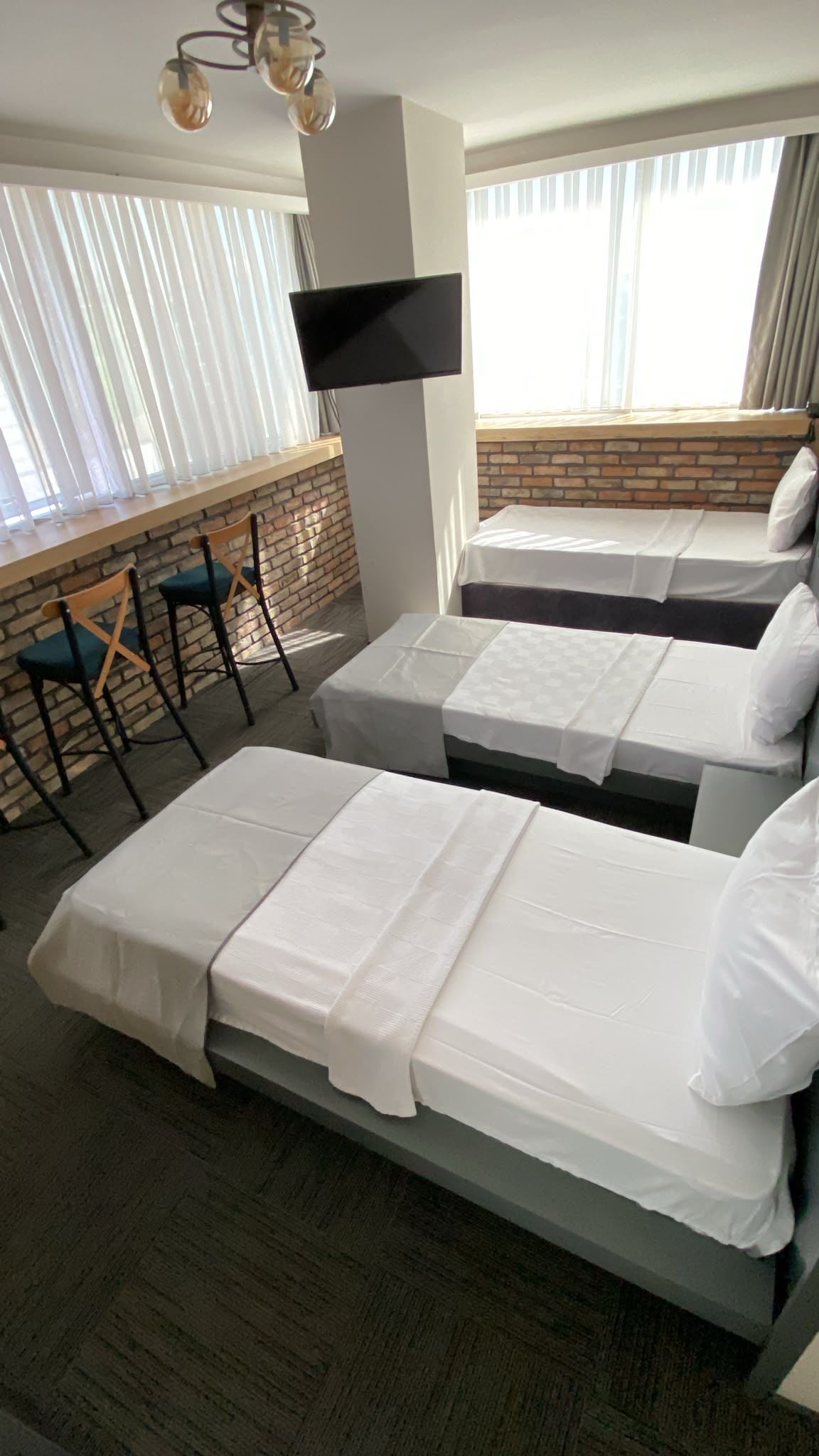 Ein Hotelzimmer mit zwei Betten, einem flachbildfernseher an der Wand, einer Ziegelwand und einem Fenster mit Vorhängen.