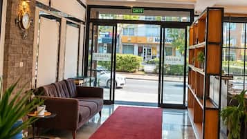 Vestíbulo de hotel con mostrador de recepción, zona de estar y vistas a la calle.