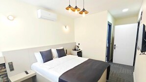 Habitación de hotel con cama, mesita de noche, lámpara, unidad de aire acondicionado y una puerta.
