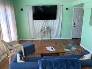 Ein Wohnzimmer mit großem Flachbildfernseher, einer Couch, einem Couchtisch und einem Korbstuhl.