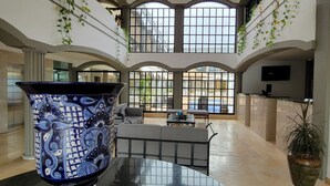 Un hall d’entrée spacieux, agrémenté d’un grand vase décoratif, d’un coin salon et offrant une vue sur l’extérieur grâce à de grandes fenêtres.