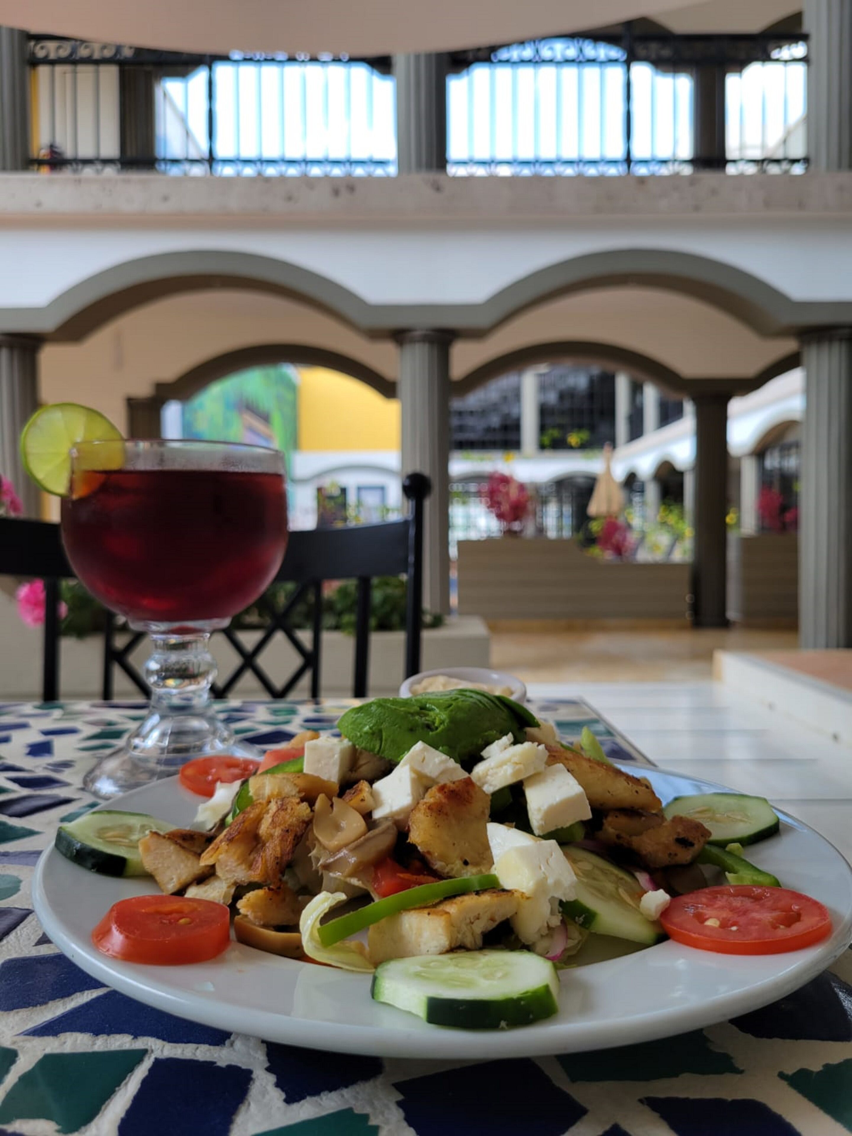 Une table avec une assiette de nourriture et une boisson, placée dans une pièce donnant sur un balcon et un espace extérieur.