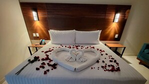 Un lit parfaitement fait, avec du linge de lit blanc, une disposition de serviettes en forme de cœur et des pétales de rose sur le lit.