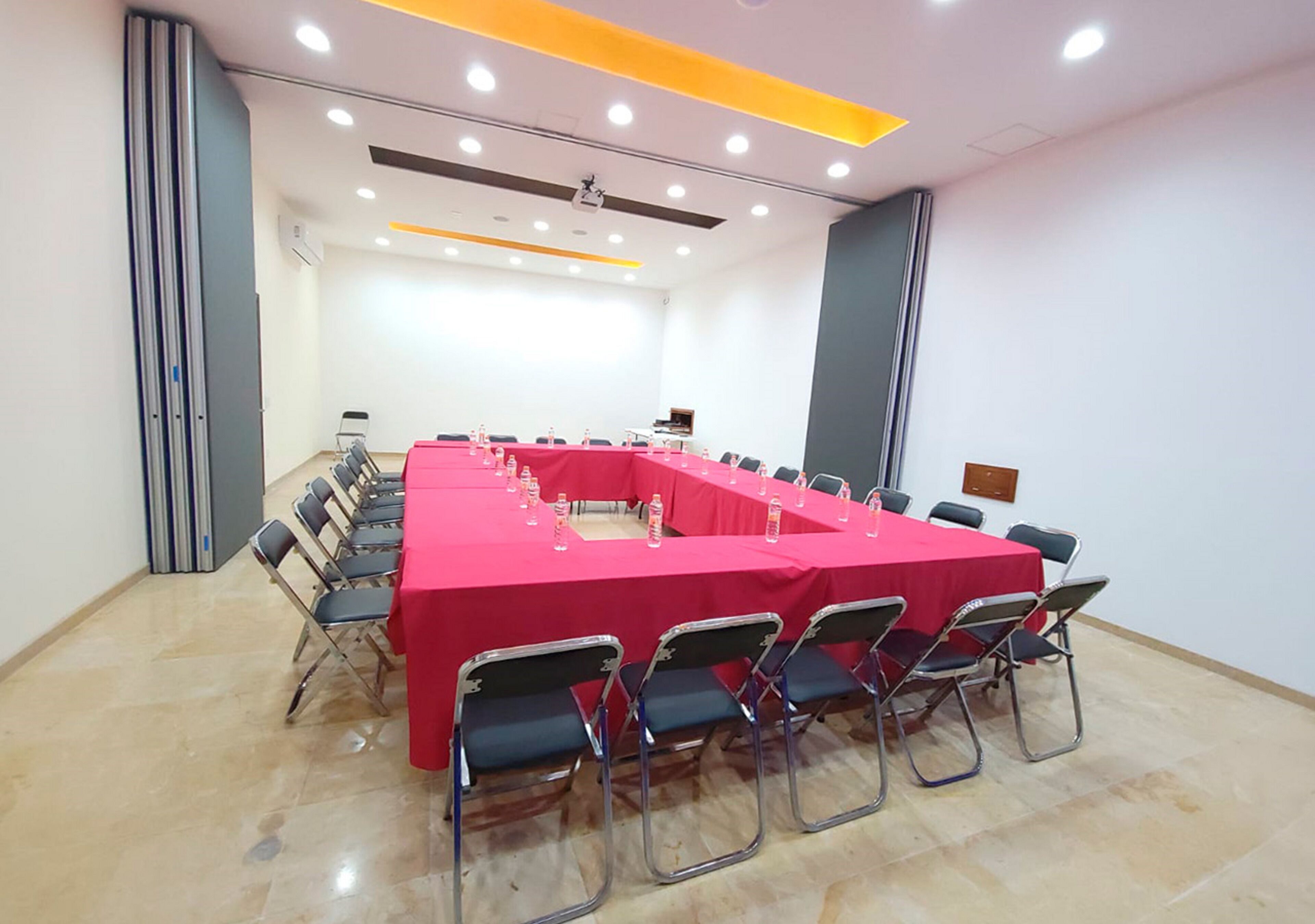 Un salón de conferencias con una larga mesa, sillas y una pantalla para proyector.