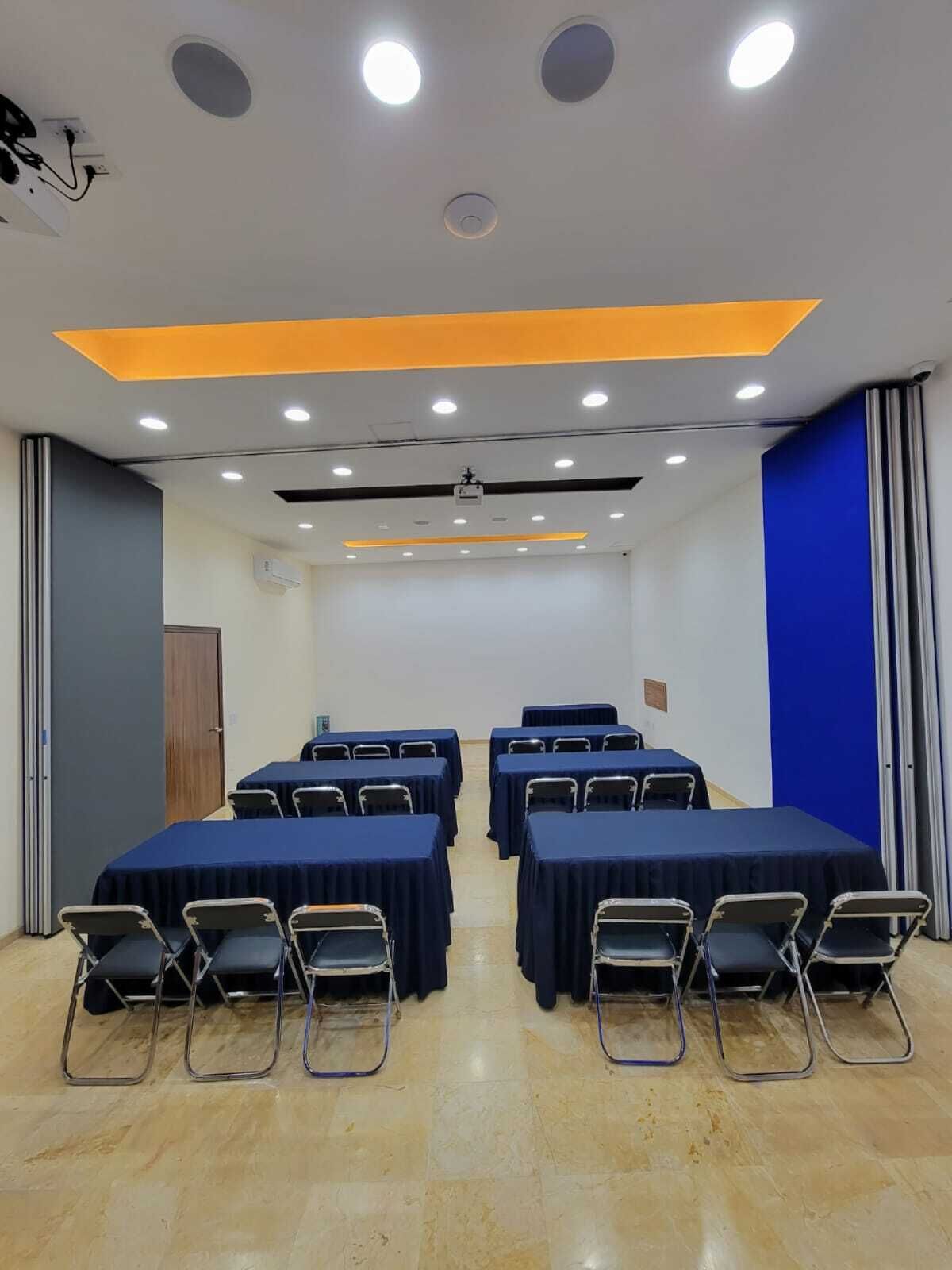 A conference room with tables and chairs, recessed lighting, and a projector on the ceiling.