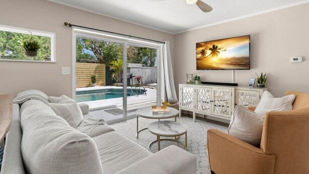 Un salon moderne avec vue sur la piscine, un ventilateur de plafond et un téléviseur fixé au mur.