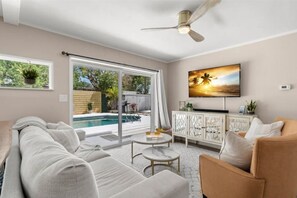 Ein modernes Wohnzimmer mit Blick auf einen Pool, einem Deckenventilator und einem an der Wand montierten Fernseher.