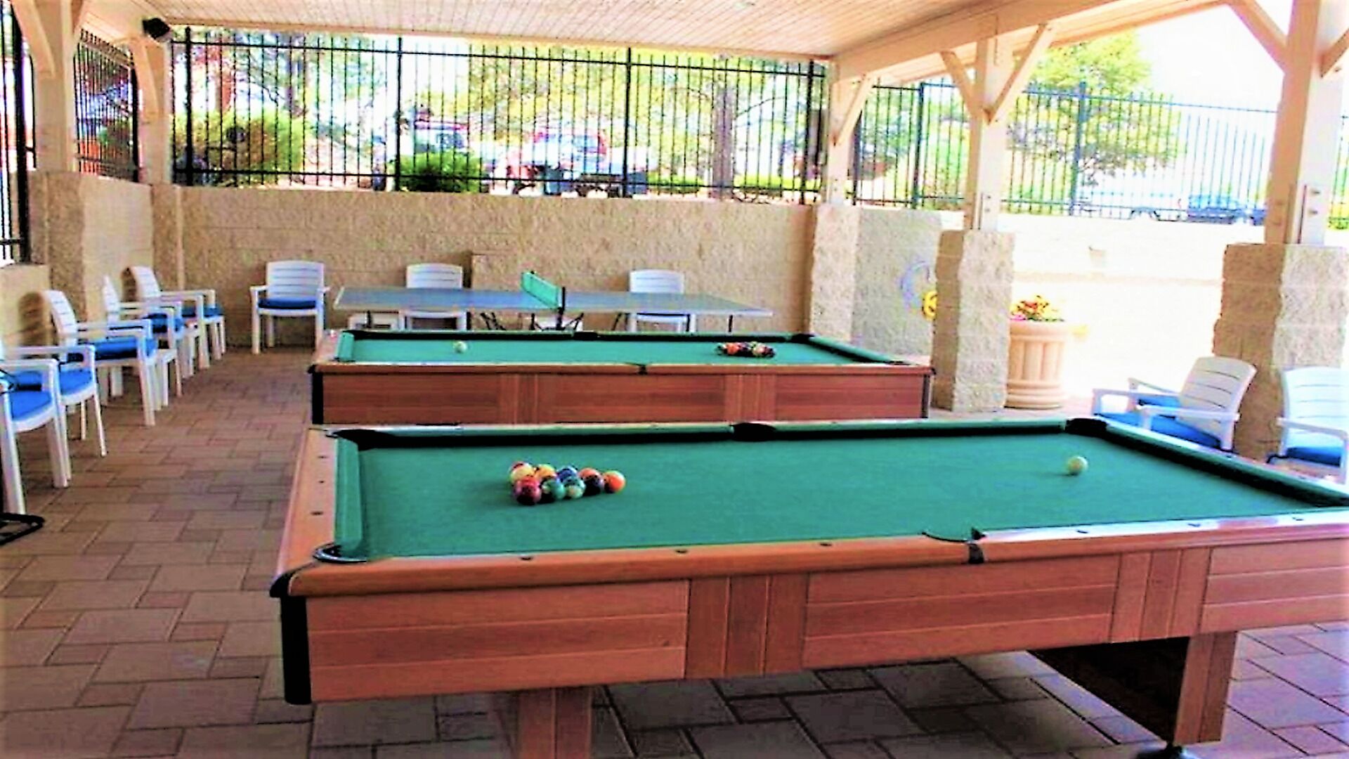 Two pool tables with chairs and a table in a covered outdoor area.