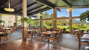 A spacious outdoor dining area with wooden tables and chairs, large windows offering a view of a golf course, and hanging pendant lights. - 2Bed/2Bath Deluxe Unit in Flagstaff! Complete w/Golf, Pools, and More! (Flagstaff)