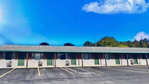 A motel with a row of rooms, a parking lot, and a clear blue sky with clouds.