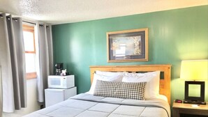 A hotel room with a bed, a bedside table with a lamp, a microwave, and a small refrigerator.
