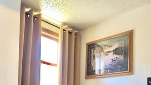 A corner room with a small table and two chairs, a framed picture on the wall, and a window with curtains.