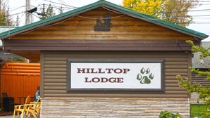 A wooden lodge with a sign reading "HILLTOP LODGE" and a logo of a bear and a tree.