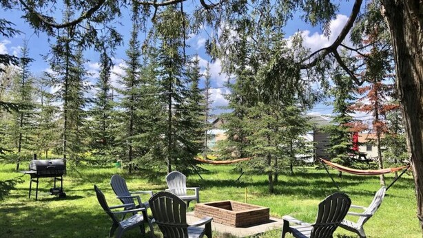 An outdoor seating area with Adirondack chairs and a fire pit, surrounded by trees and a hammock.
