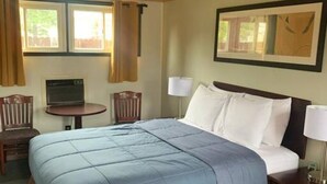 A hotel room with a large bed, a desk, a chair, and a window with curtains.