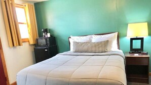A hotel room with a large bed, a bedside table with a lamp, a small table with a coffee maker, and a TV on the table.