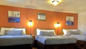 A hotel room with two beds, each with a headboard, a bedside table, and a lamp. There is an air conditioning unit on the wall.