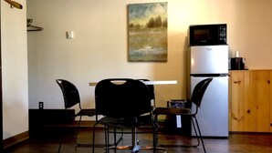 A small kitchen with a white refrigerator, a microwave, and a painting on the wall. There are two black chairs and a table.
