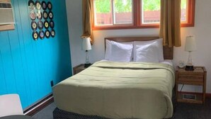 A bedroom with a bed, a window with curtains, a wall with a record collection, and a small table. - Hilltop Lodge Standard Queen - Room 101 (International Falls)