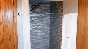Une douche avec un mur carrelé, une porte en bois et une serviette blanche accrochée au mur.