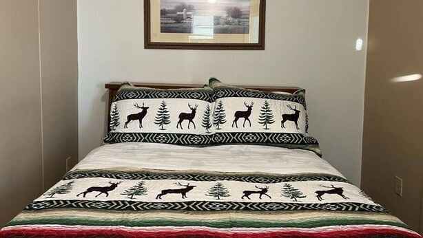 Una cama con una colcha estampada que muestra ciervos y árboles, un cuadro enmarcado sobre la cama y un cabecero de madera.