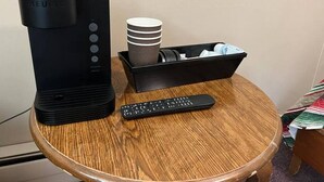 Una cafetera Keurig sobre una mesa de madera, con un control remoto y una pila de tazas blancas.